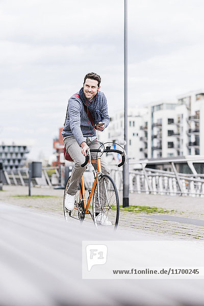 Businessman riding bicycle in the city  while using smartphone and earphones