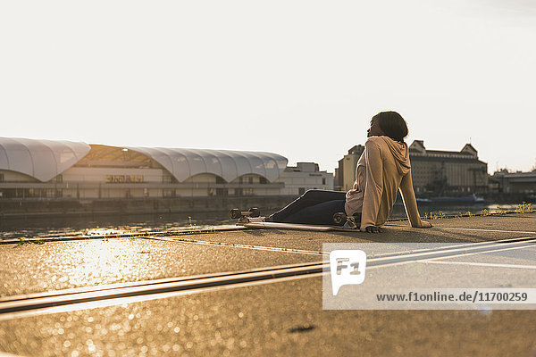 Junge Frau sitzt am Fluss und beobachtet den Sonnenuntergang.