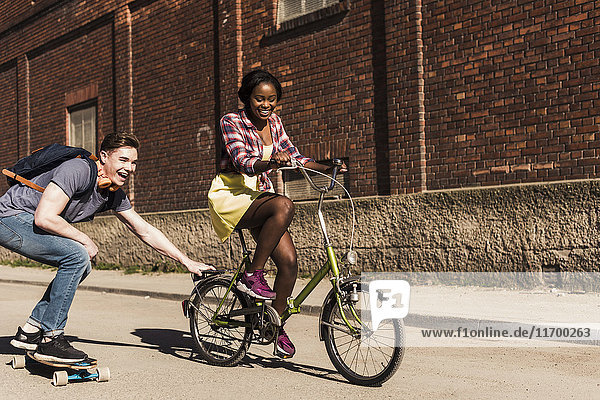 Young woman on bicycle pulling young man  standing on skateboard