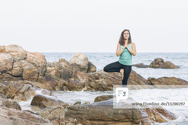 Frau beim Yoga auf einem Felsen am Meer
