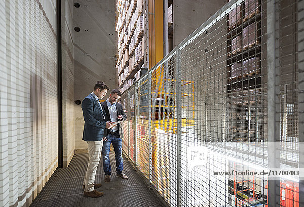 Two men in automatized high rack warehouse looking at tablet