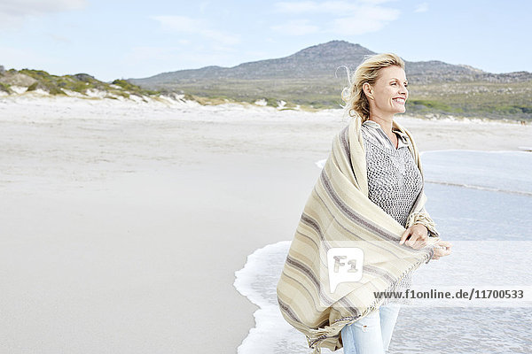 Mature woman enjoying the sea  wrapped in a blanket