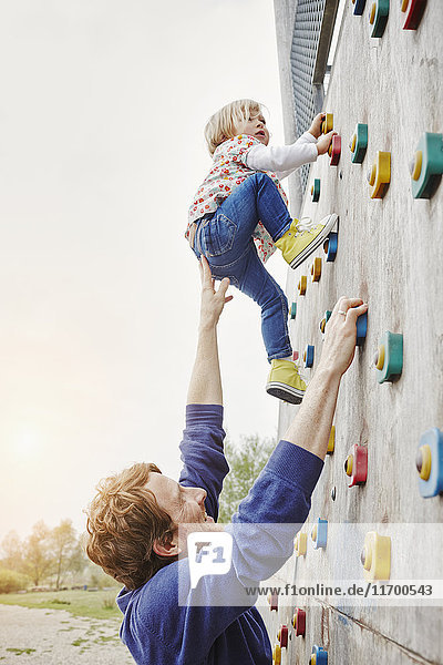 Girl climbing on a wall supported by father