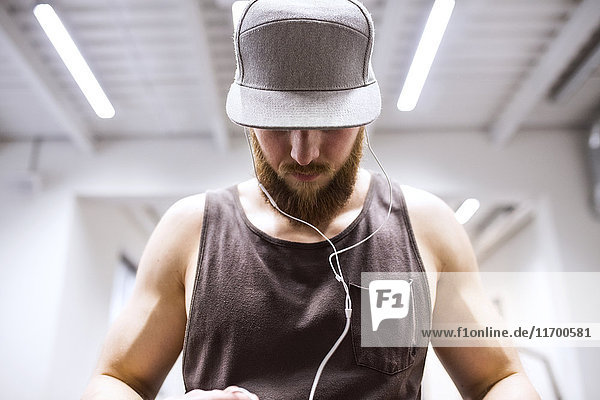 Junger Sportler mit Mütze  mit Kopfhörer im Fitnessstudio