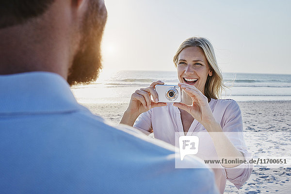 Glückliche Frau beim Fotografieren des Mannes am Strand
