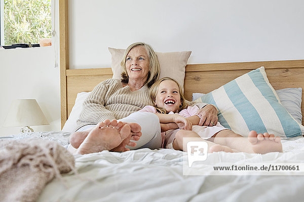 Laughing little girl lying on the bed with her grandmother