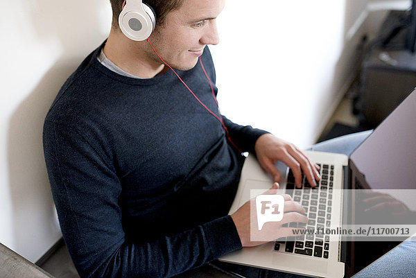 Mann mit Laptop und Kopfhörer zu Hause