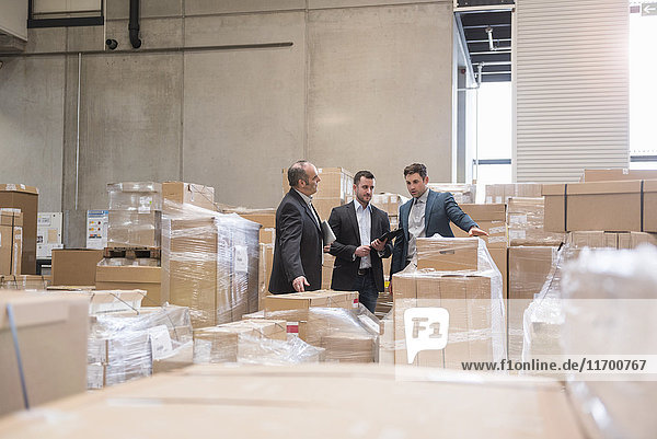 Three men in factory warehouse surrounded by cardboard boxes
