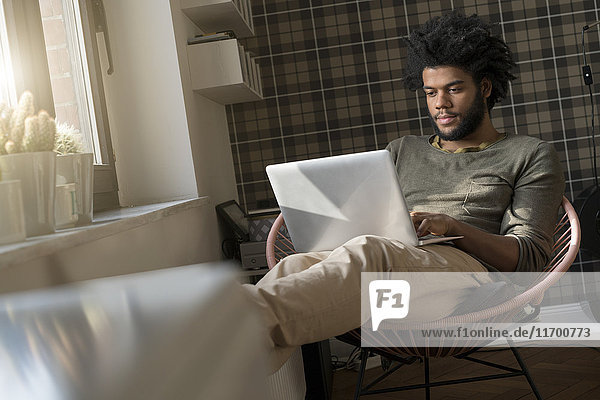 Man sitting in living room in armchair working on laptop