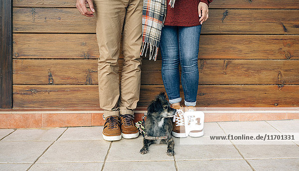 Low section of couple with dog standing in front of wooden wall
