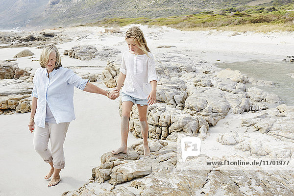 Großmutter und Enkelin gehen am Strand spazieren und halten Händchen.