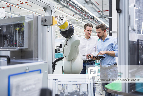 Two men with tablet examining assembly robot in factory shop floor