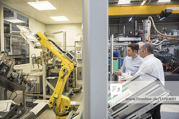 Zwei Männer  die in der Fabrikhalle reden und einen Industrieroboter anschauen.