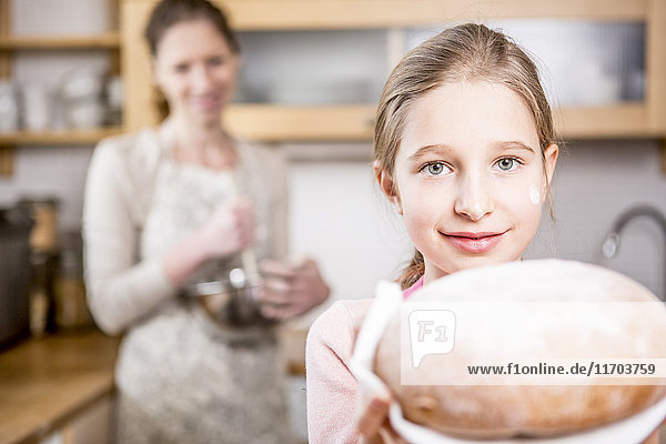 Mädchen mit Brot in der Küche mit Mutter im Hintergrund