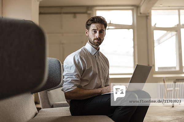 Portrait eines jungen Geschäftsmannes mit Laptop im Loft