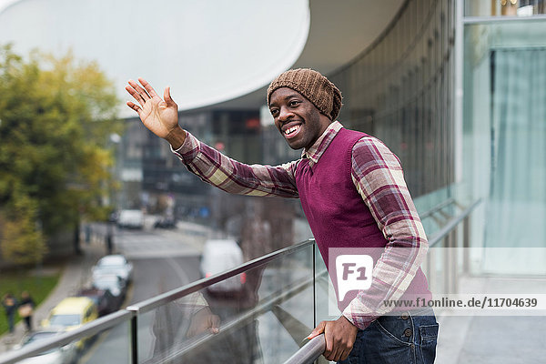Portrait of smiling man standing on terrace waving while looking at distance