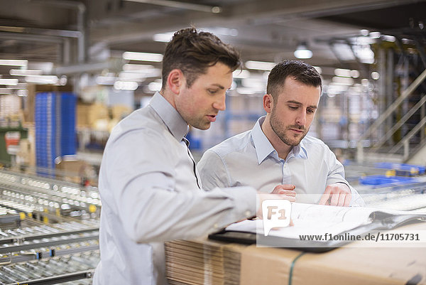 Two men in factory warehouse looking at documents