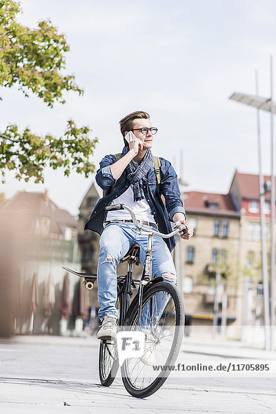 Junger Mann mit Fahrrad in der Stadt telefoniert mit dem Handy
