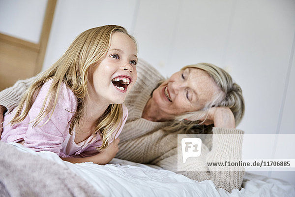 Porträt eines lachenden kleinen Mädchens  das mit seiner Großmutter auf dem Bett liegt.