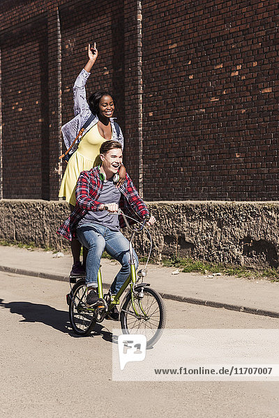 Young man riding bicycle with his girlfriend standing on rack