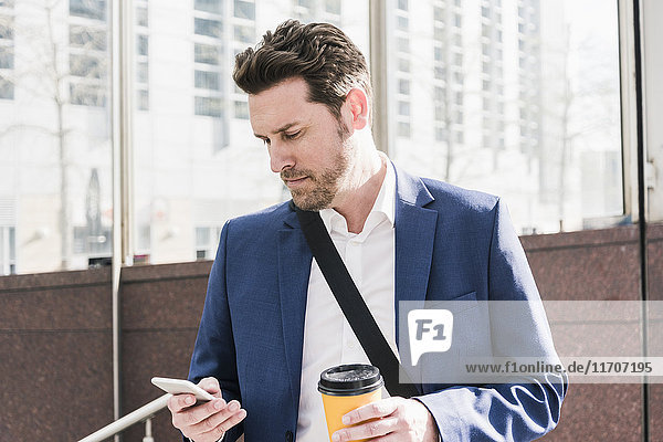 Geschäftsmann in der Stadt  liest Smartphone Nachrichten und hält eine Tasse Kaffee.