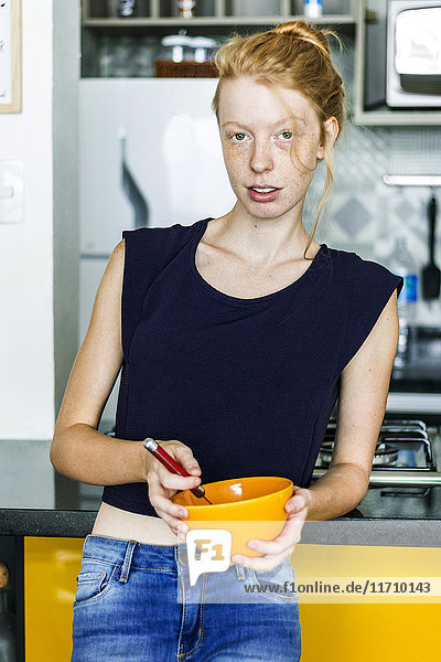Ginger woman standing in kitchen eating breakfast