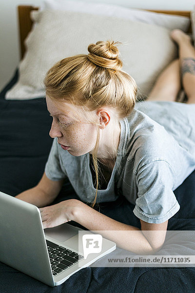 Young woman lying on couch using laptop