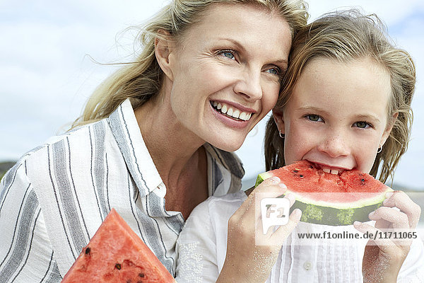 Mother and daughter eating water melon on the beach