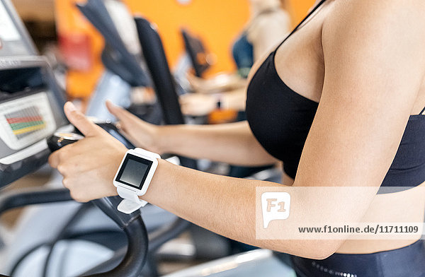 Frau im Fitnessstudio mit smartwatch mit einem Ellipsentrainer