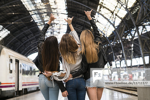 Back view of three young women standing arm in arm on platform