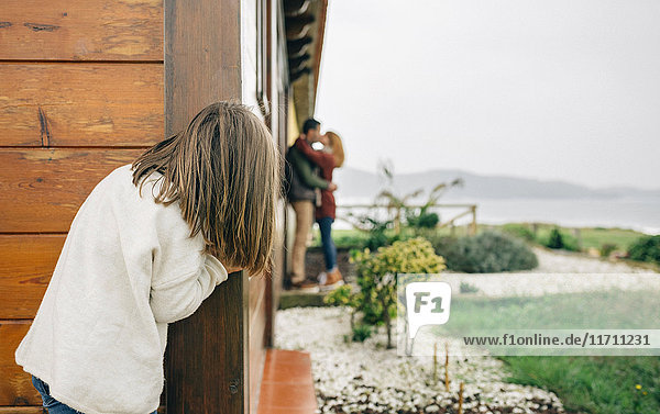 Back view of little girl spying couple in love kissing next to wooden house