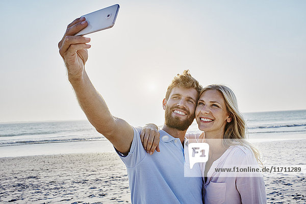 Ein glückliches Paar mit einem Selfie am Strand