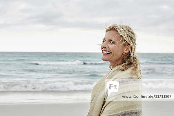 Mature woman enjoying the sea  wrapped in a blanket