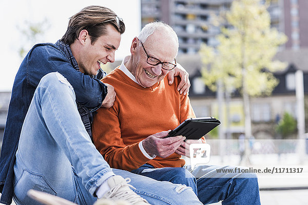 Happy senior man and adult grandson looking at tablet