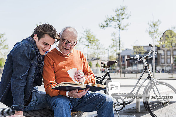 Senior Mann und erwachsener Enkel auf einer Bank beim Betrachten des Fotoalbums