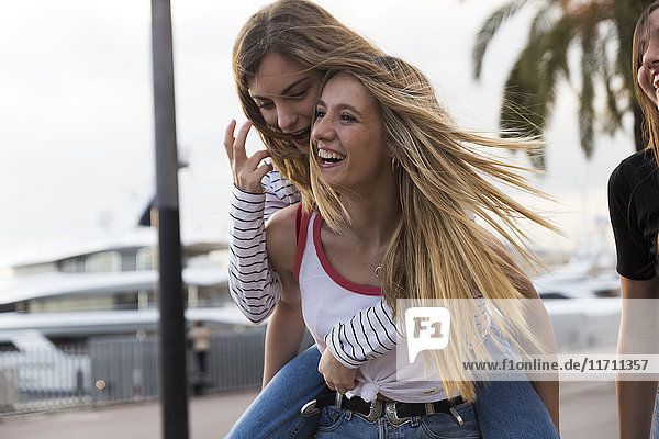Laughing young woman giving her friend a piggyback ride