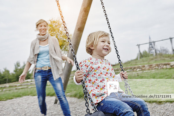 Mother with daughter on swing on playground