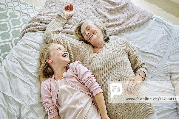 Little girl lying on the bed with her grandmother having fun
