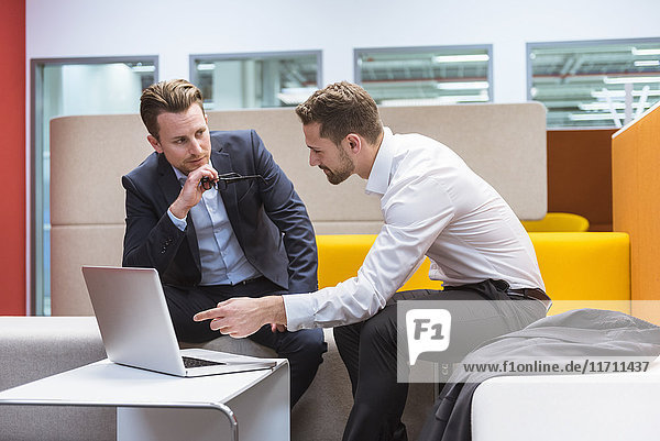 Businessmen sitting in conversation pit  discussing in front of laptop