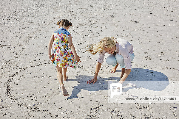 Mutter und Tochter beim Zeichnen des Herzens am Strand
