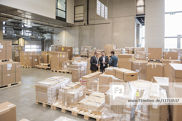 Three men in factory warehouse surrounded by cardboard boxes