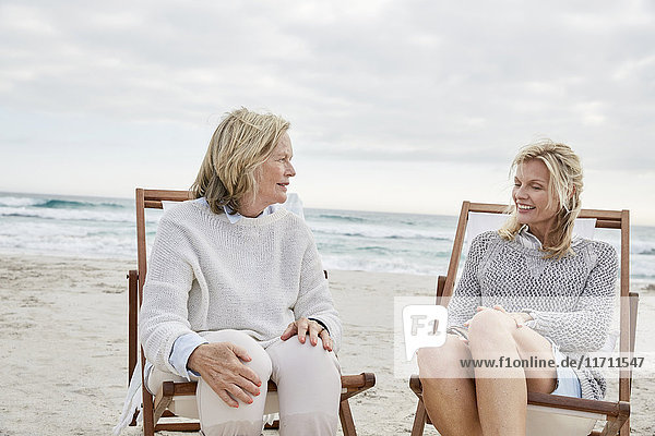 Mutter und Tochter sprechen am Strand und sitzen in Liegestühlen.