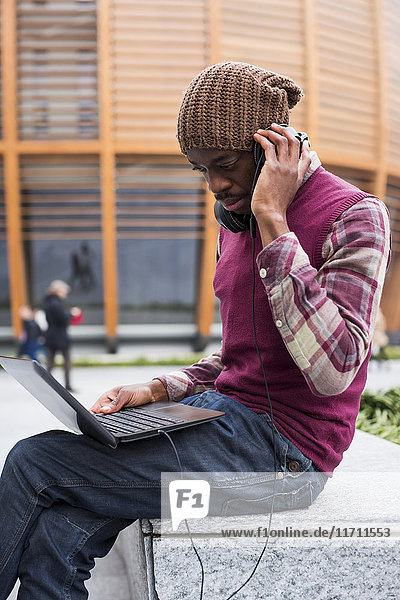 Mann auf der Bank sitzend mit Kopfhörern beim Blick auf den Laptop