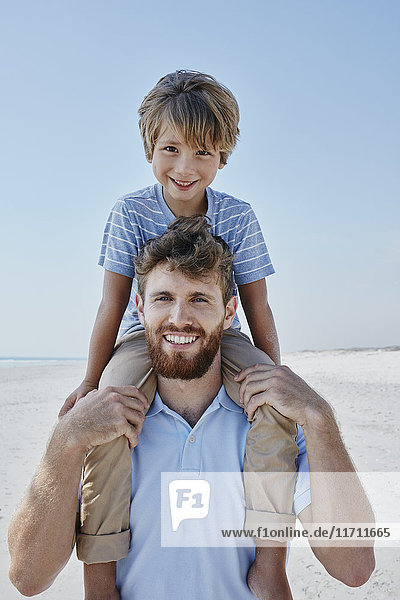 Portrait of father carrying son piggyback on the beach