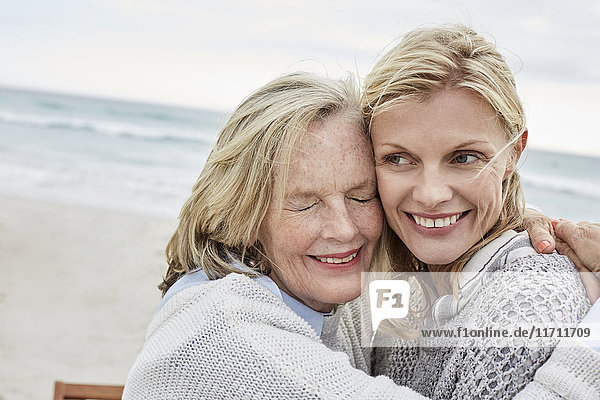 Mutter und Tochter umarmen sich am Strand