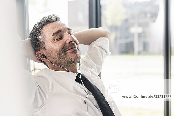 Portrait eines lächelnden Geschäftsmannes mit geschlossenen Augen Musik hören mit Kopfhörern