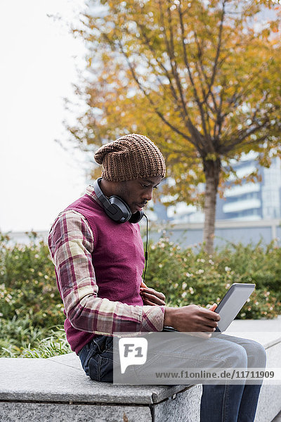 Mann mit Kopfhörer auf der Bank sitzend  mit Blick auf den Laptop