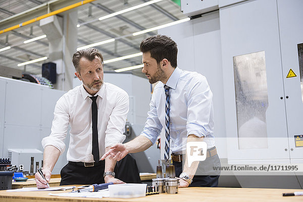 Two businessmen at table in factory shop floor discussing