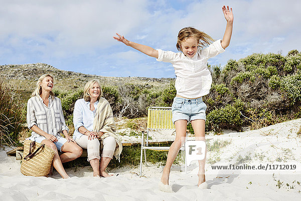Mutter,  Tochter und Großmutter verbringen einen Tag am Strand,  Mädchen springen vor Freude