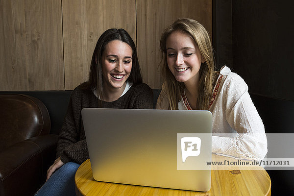 Two smiling friends sitting in a coffee shop looking at laptop